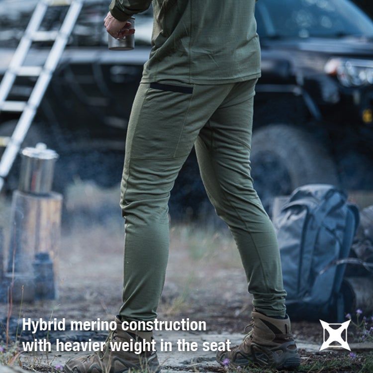 Product Photography: Person wearing olive green merino wool pants near a campfire with a ladder and vehicle in the background featuring a dark gray backpack and brown hiking boots