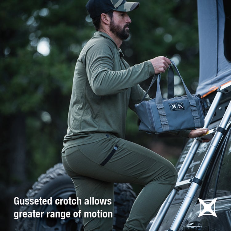 A photograph shows a man in olive green clothing carrying a gray duffel bag while climbing a ladder on a vehicle in a lush green forest, featuring a camo hat, a silver ladder and the man's beard