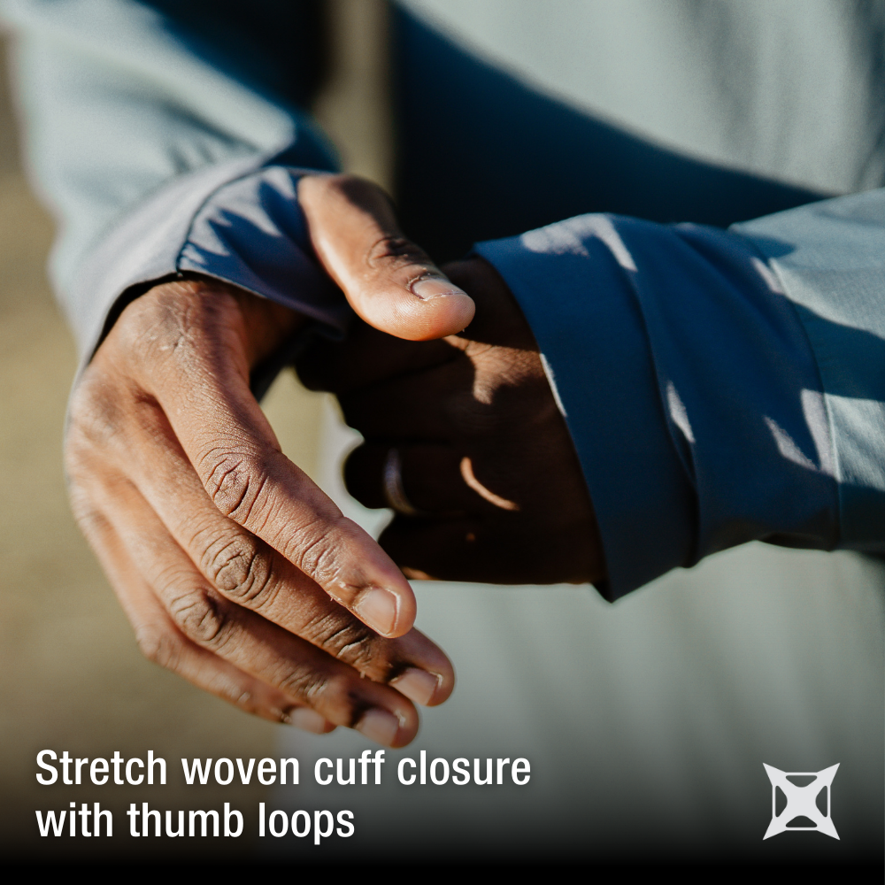 Close-up photograph showing a person's hands demonstrating stretch woven cuff closure with thumb loops featuring detailed skin texture and a subtle ring detail against a blurred outdoor background