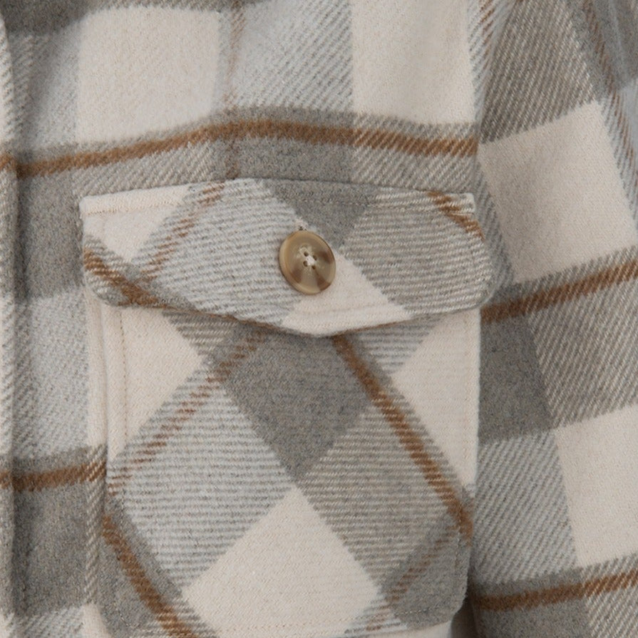 Close-up of a grey and beige plaid flannel shirt featuring a single buttoned pocket and subtle brown lines