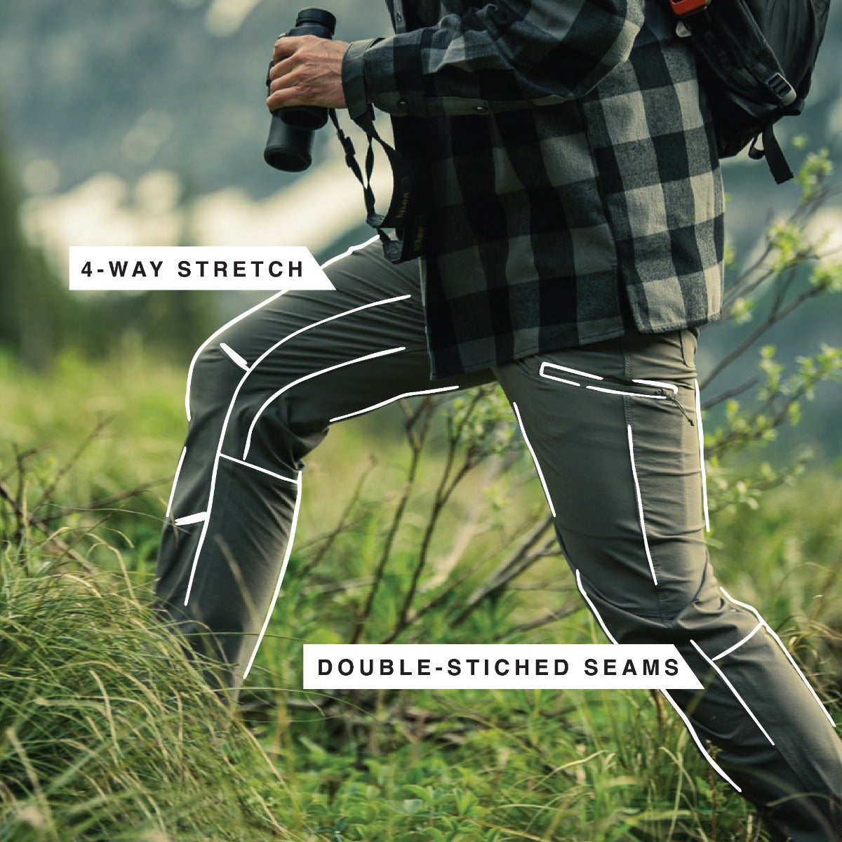 Photograph of a person wearing olive green hiking pants with double-stitched seams and multiple pockets hiking amidst tall grass against a backdrop of majestic mountains featuring a gray and black plaid shirt and binoculars showcasing the pants 4-way stretch