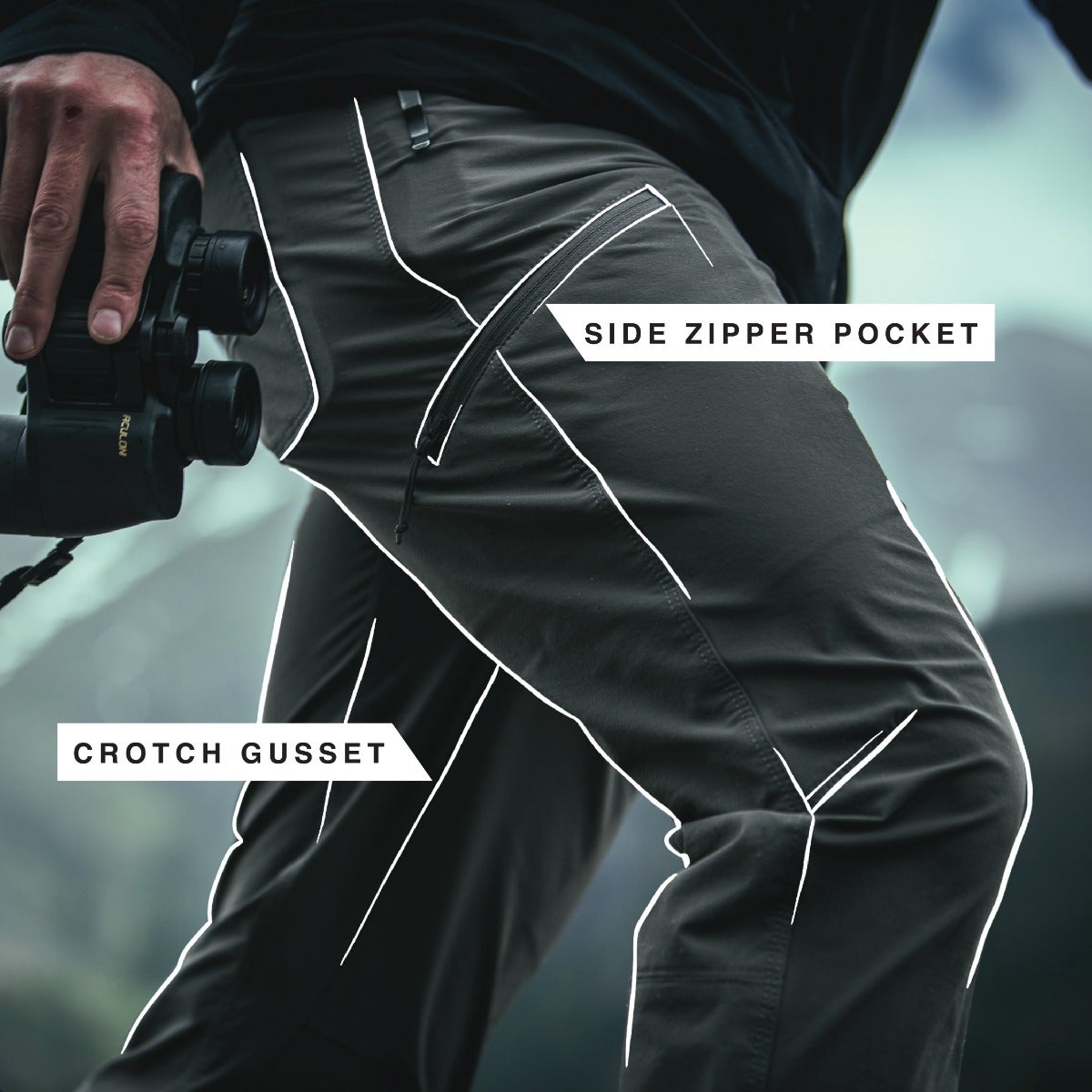 Product shot featuring a person wearing dark gray hiking pants with side zipper pockets and a crotch gusset against a blurry mountain backdrop showcasing the pants' functionality and design details
