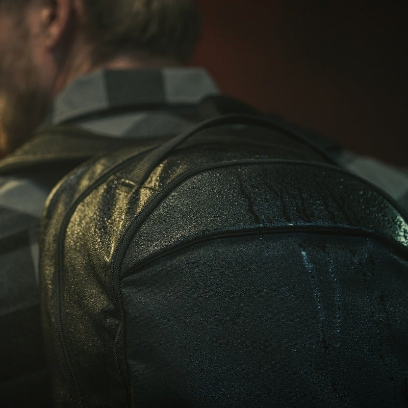 Close-up photography of a dark-colored, water-resistant backpack with visible water droplets, showcasing its textured fabric and sleek design details.