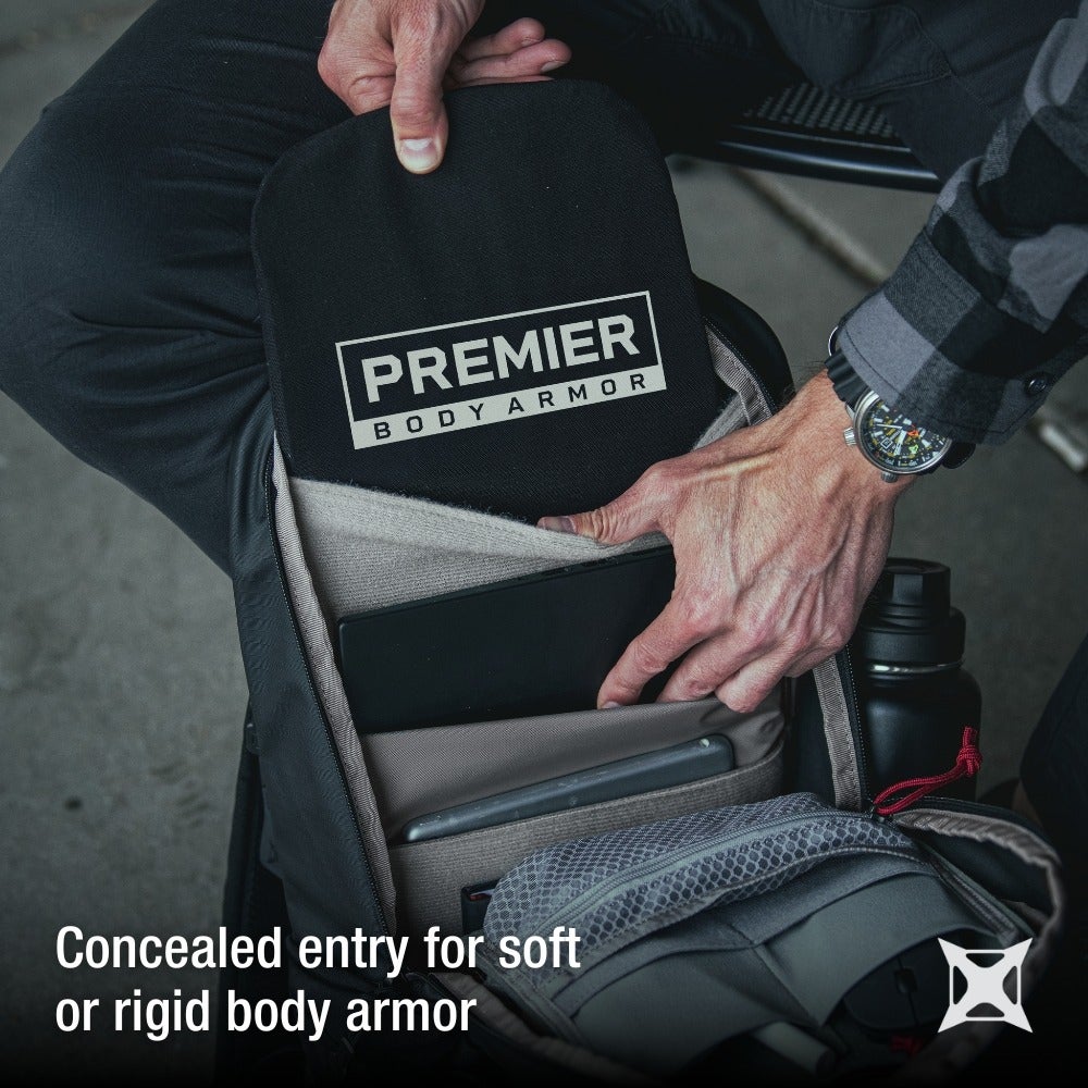 Premier Body Armor product photo showing a person placing a black ballistic plate into a backpack with other items such as a tablet and water bottle the plate features the Premier Body Armor logo in beige lettering the interior of the pack shows beige and gray fabric compartments