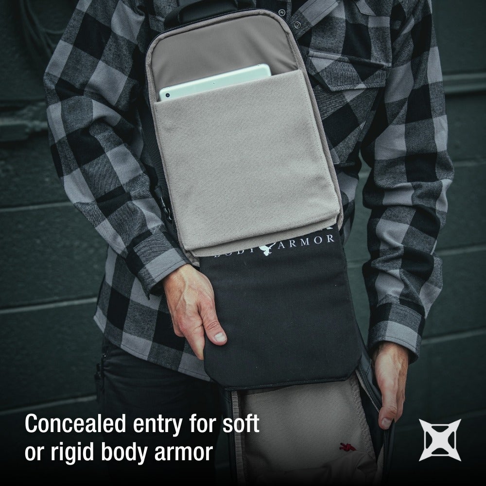 Body Armor product photography showing a person revealing a concealed compartment in a gray and black backpack against a dark background with a tablet visible inside featuring a soft beige interior and a subtle logo
