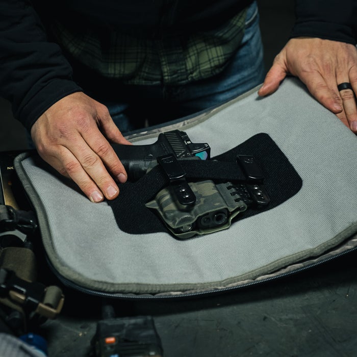 Photograph showing a Glock handgun in a camouflage holster secured with a black strap inside a gray padded carrying case