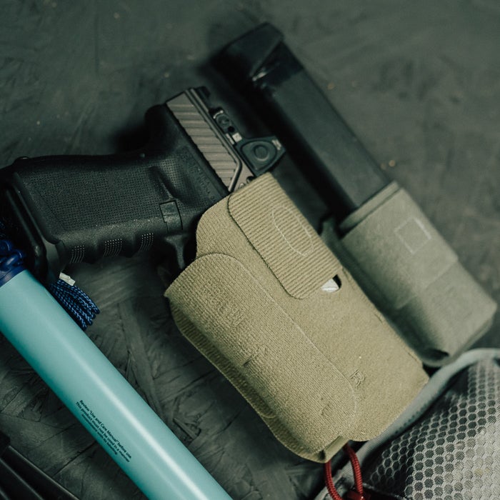 Photograph showing a Glock handgun in a tan holster with a spare magazine and a teal water filter a dark gray textured background