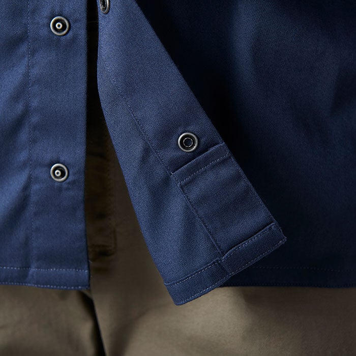 Close-up of a navy blue cotton shirt showing details like a buttoned cuff and a small pocket, featuring subtle stitching and dark metal buttons