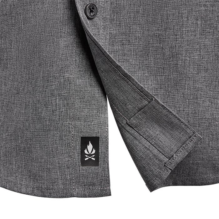 Close-up of a charcoal gray heathered performance shirt showing a small black logo of a campfire and crossed oars a button and a unique hidden pocket detail