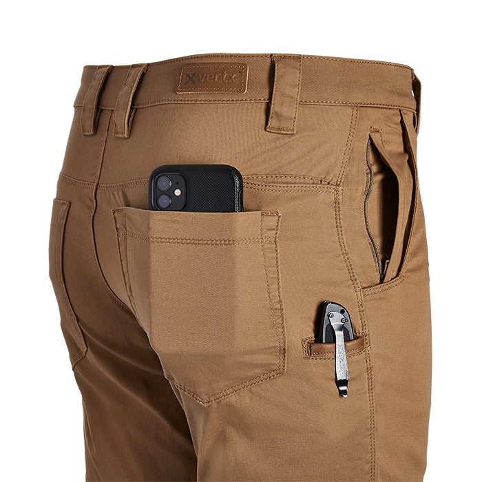 Product shot of Vertex pants showing a tan fabric a black phone in a back pocket and a small multi-tool in a side pocket with contrasting stitching details