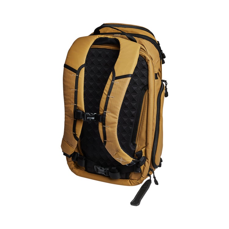 Product shot of a tan and black Dakine backpack featuring a padded back panel, adjustable straps, and a unique lower strap detail