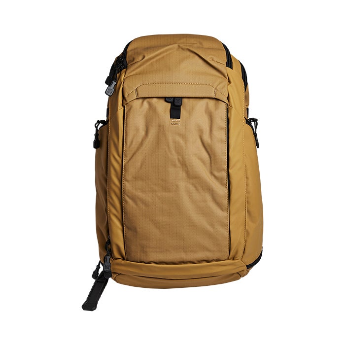 Product shot of a tan Peak Design Travel Backpack with black accents showing its zippered compartments and adjustable straps