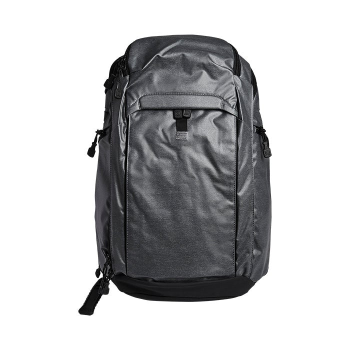 Product shot of a dark gray and black ballistic nylon backpack with compression straps and a subtle sheen against a white background