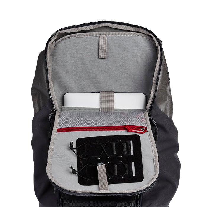 Product shot of a dark gray backpack interior showing a laptop sleeve, red zippered mesh pocket, and a gray organizer with black elastic straps