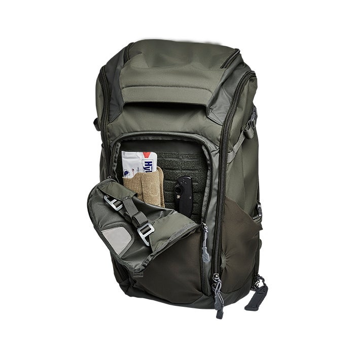 Product shot of a dark olive-green backpack with multiple compartments showing a knife, tan pouch and first-aid packet inside featuring grey accents and adjustable straps