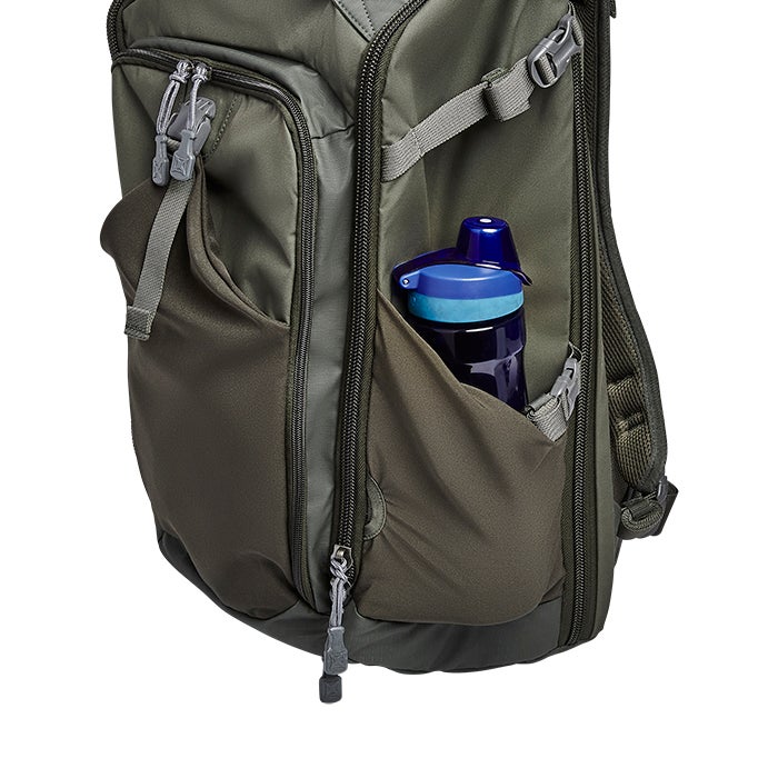 Product shot showing a green backpack with an external pocket containing a blue water bottle featuring gray zippers and dark gray pull tabs