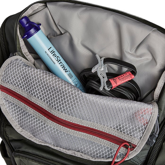 Product shot showing the interior of a green backpack with a Lifstraw water filter, a grey mesh pocket, and a red and black tourniquet