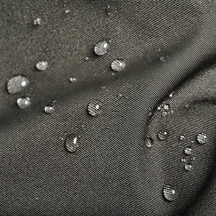 Close-up photograph showing water droplets on a dark-green, subtly textured fabric showcasing its water-resistant properties the droplets are clear and spherical reflecting light