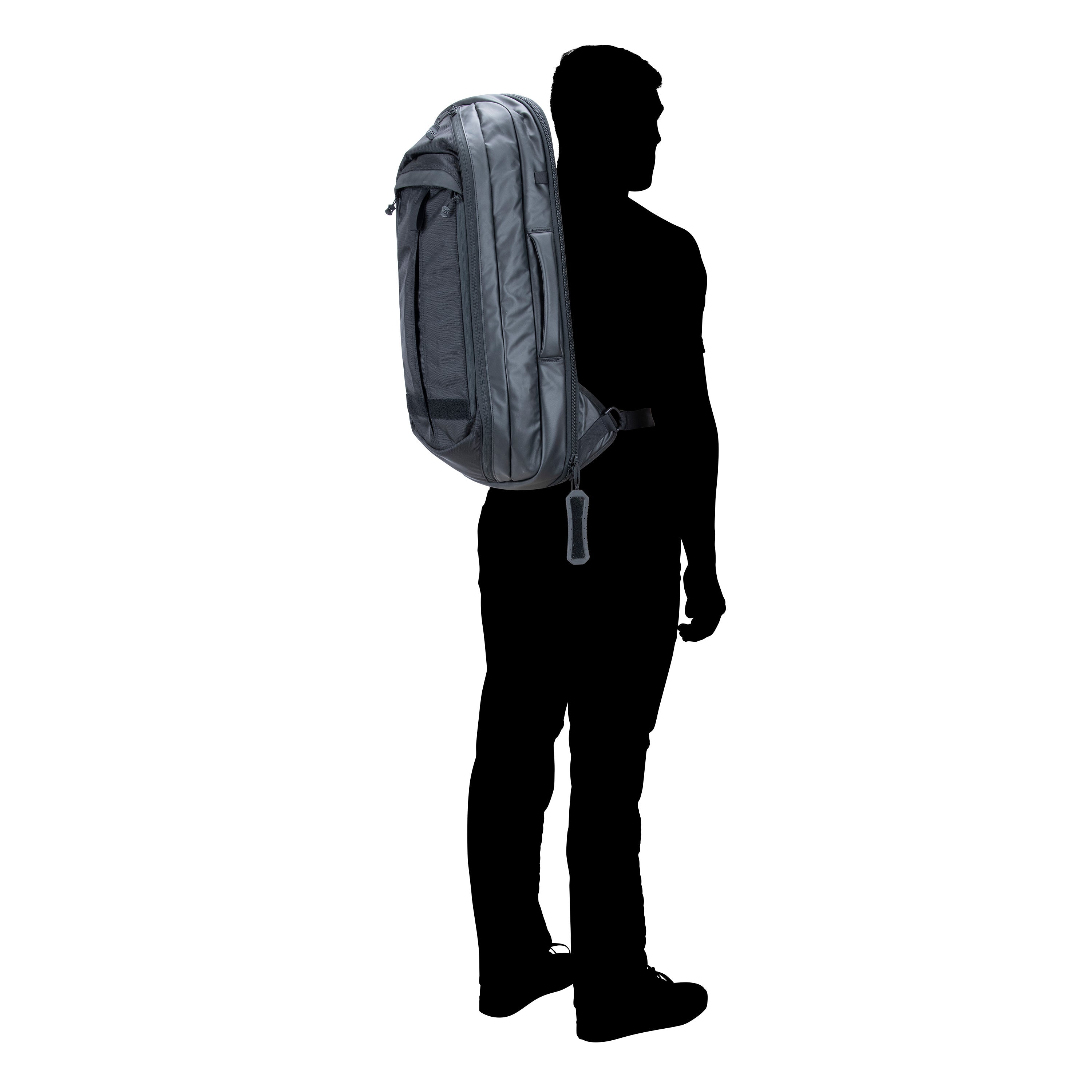 Silhouette photograph of a person with a dark gray backpack featuring a unique zipper pull and side compression straps against a white background