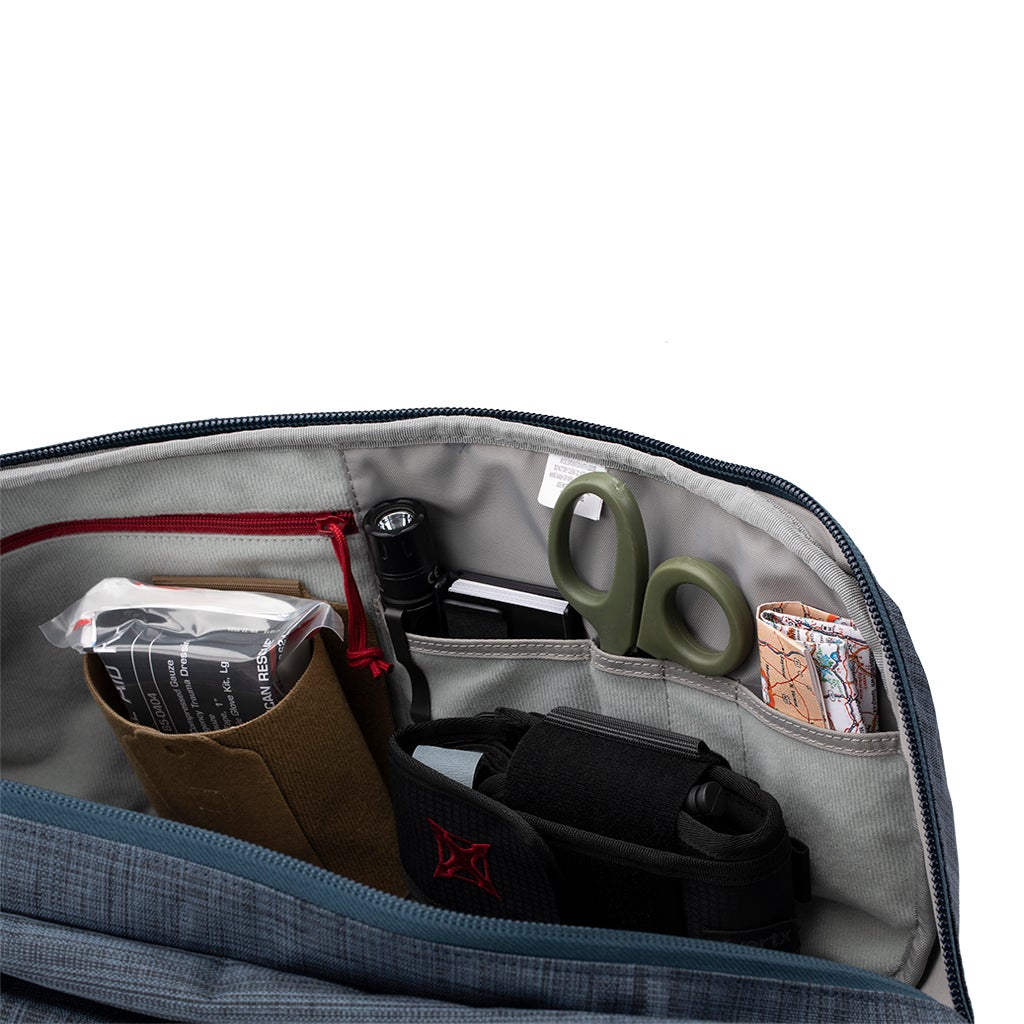 Product photography showing the interior of a blue bag with organized compartments containing a flashlight, olive green scissors, a rolled-up map, and a tan first aid kit.