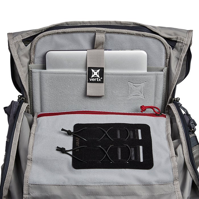 Product shot showing the interior of a Vertx backpack featuring a padded laptop sleeve gray felt lining red zipper and black modular webbing