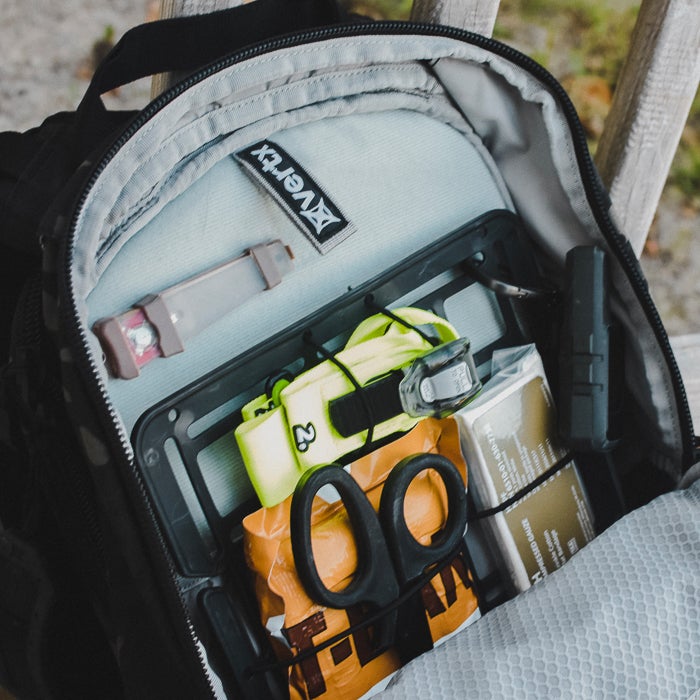 Photograph showing the inside of a black Vertex backpack containing medical supplies a lime green strap black shears and an orange package