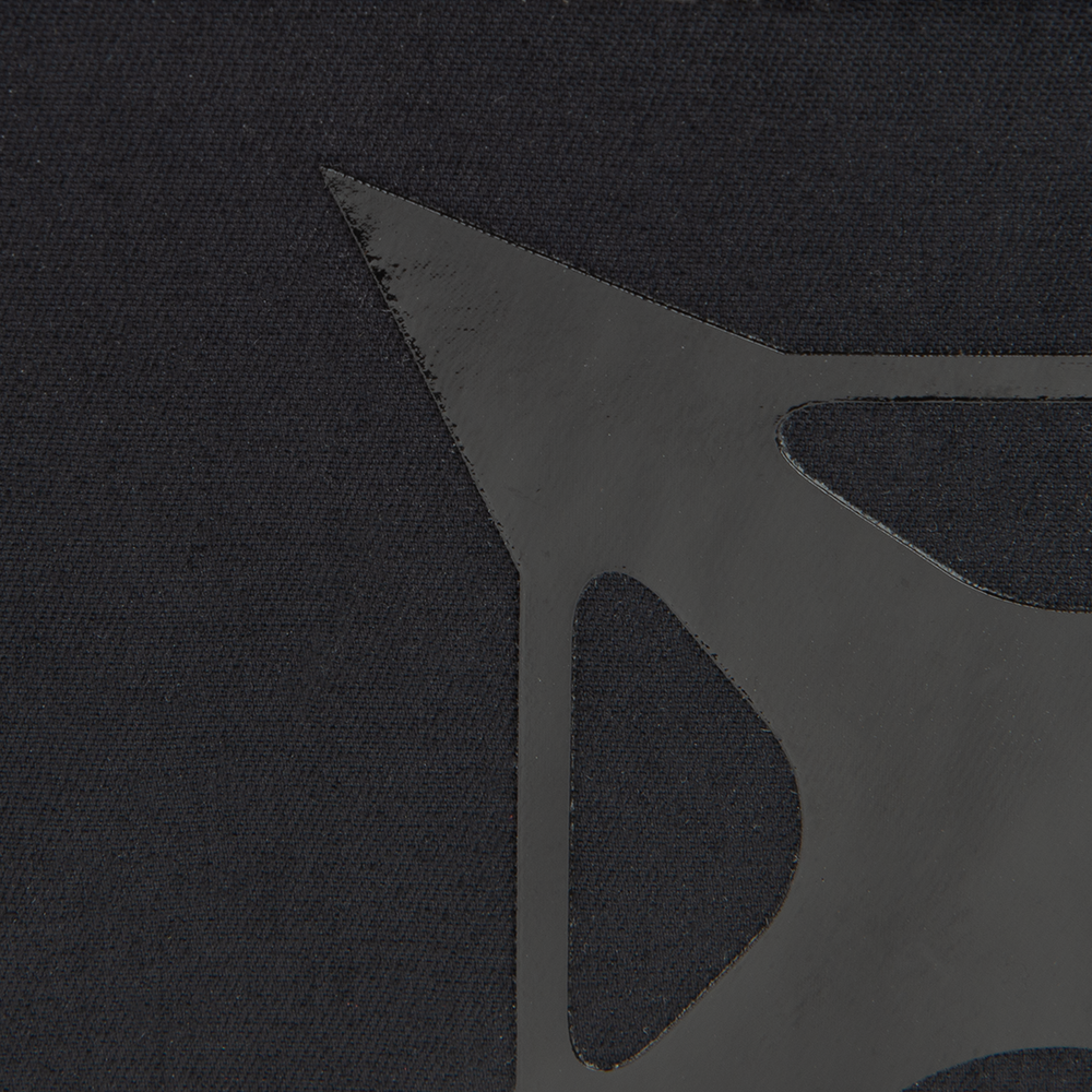 Close-up detail of a black textile with a glossy, geometric, star-shaped design featuring sharp angles and smooth curves on a textured background