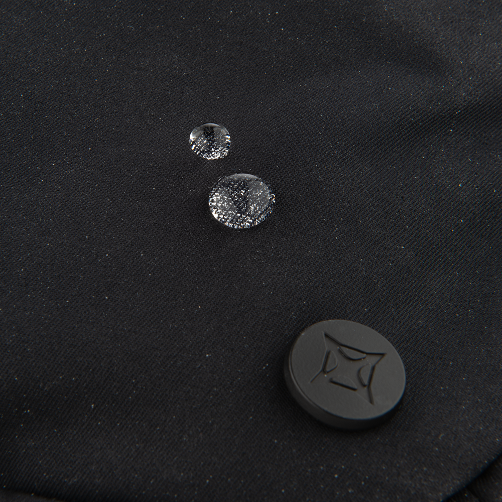 Close-up product shot showing water beading on dark fabric with a black circular logo and speckled texture