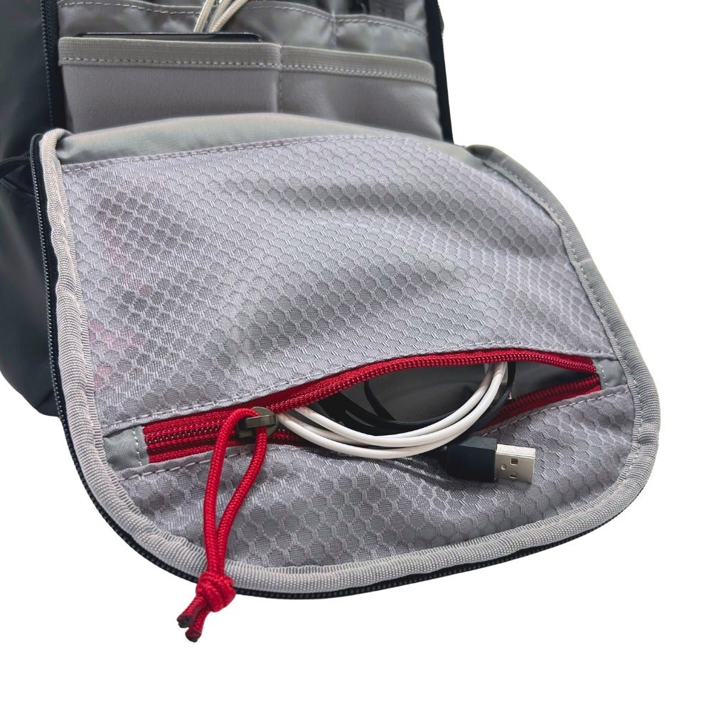 Close-up product shot of a black travel organizer featuring a gray mesh pocket with red zipper and cord detail showing USB cables neatly stored inside