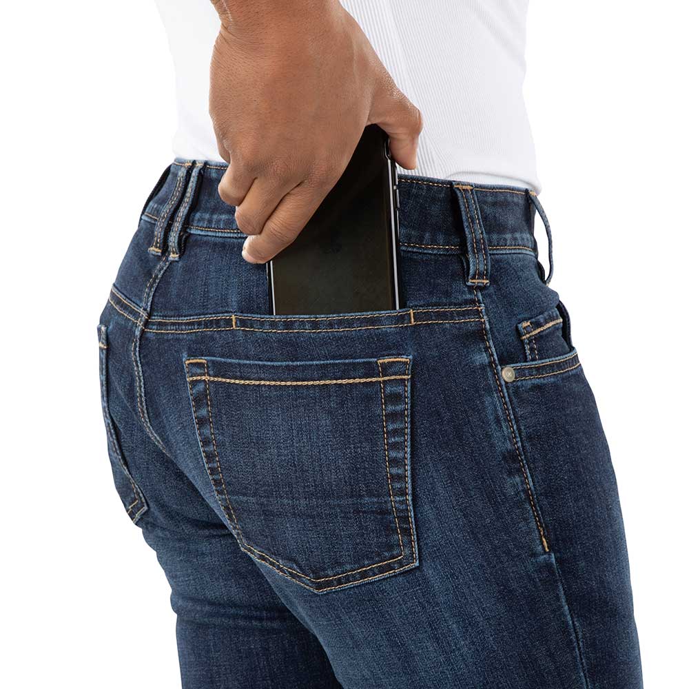 Studio photography of a person placing a black smartphone in the back pocket of dark wash jeans featuring contrast stitching and a small coin pocket