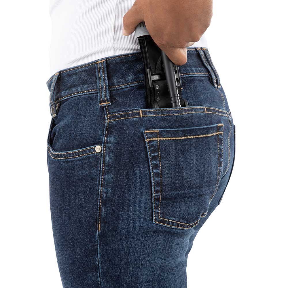 Product shot showing a person placing a black tactical pen in the back pocket of dark wash jeans featuring contrast stitching and a button detail
