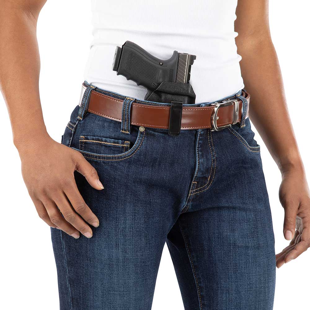 Product shot showing a person wearing dark wash jeans a brown leather belt and a black handgun in a concealed holster at the waist