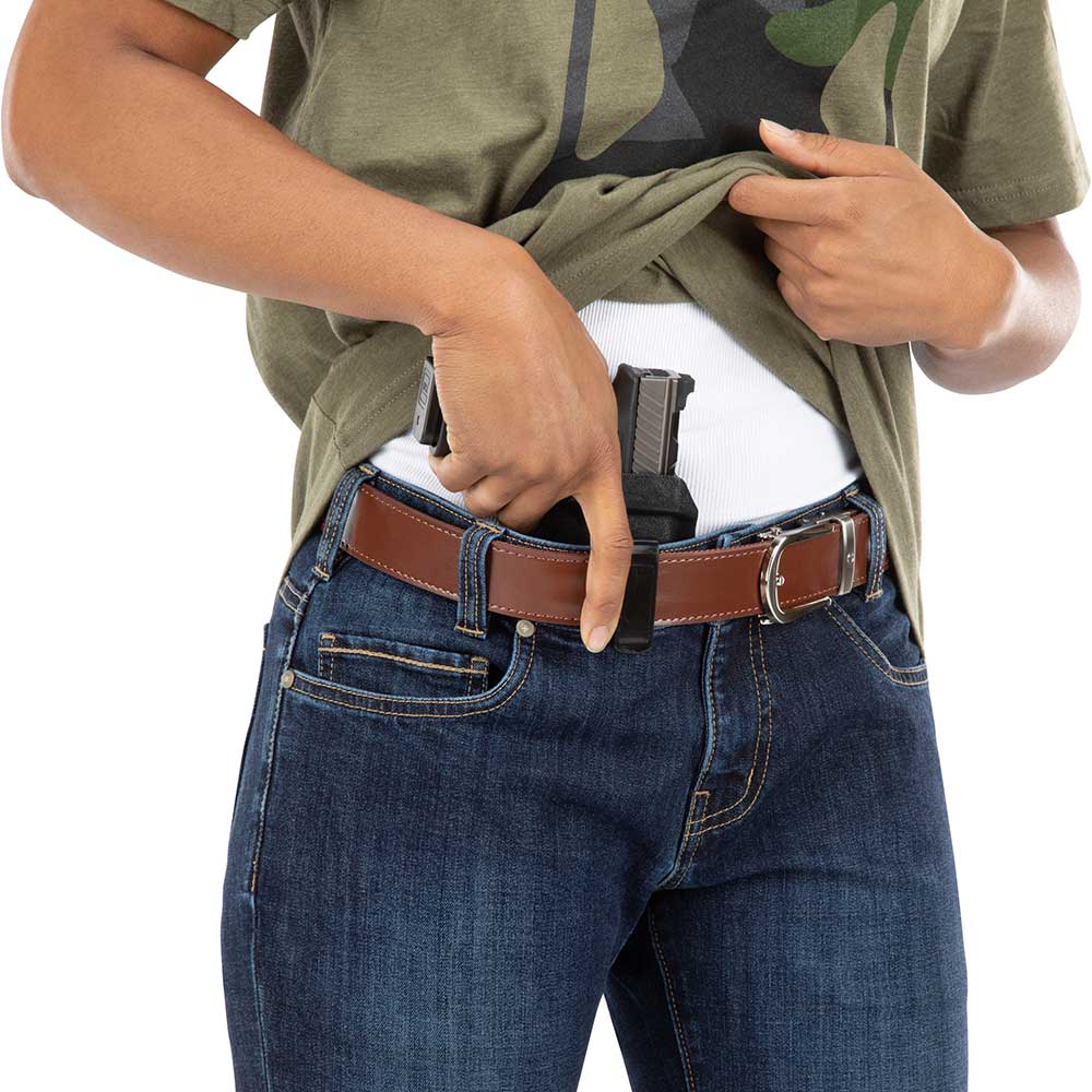 Product shot showing a person wearing dark wash jeans a brown leather belt and a concealed firearm in a black holster a green shirt is partially visible
