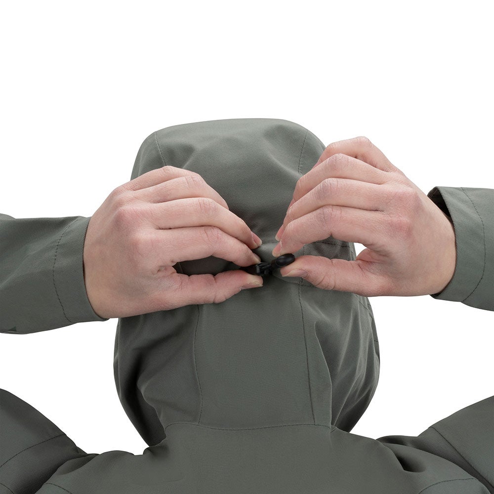 Product shot showing hands adjusting the hood of a sage-green jacket featuring a unique cinch closure with black toggles and subtle stitching details