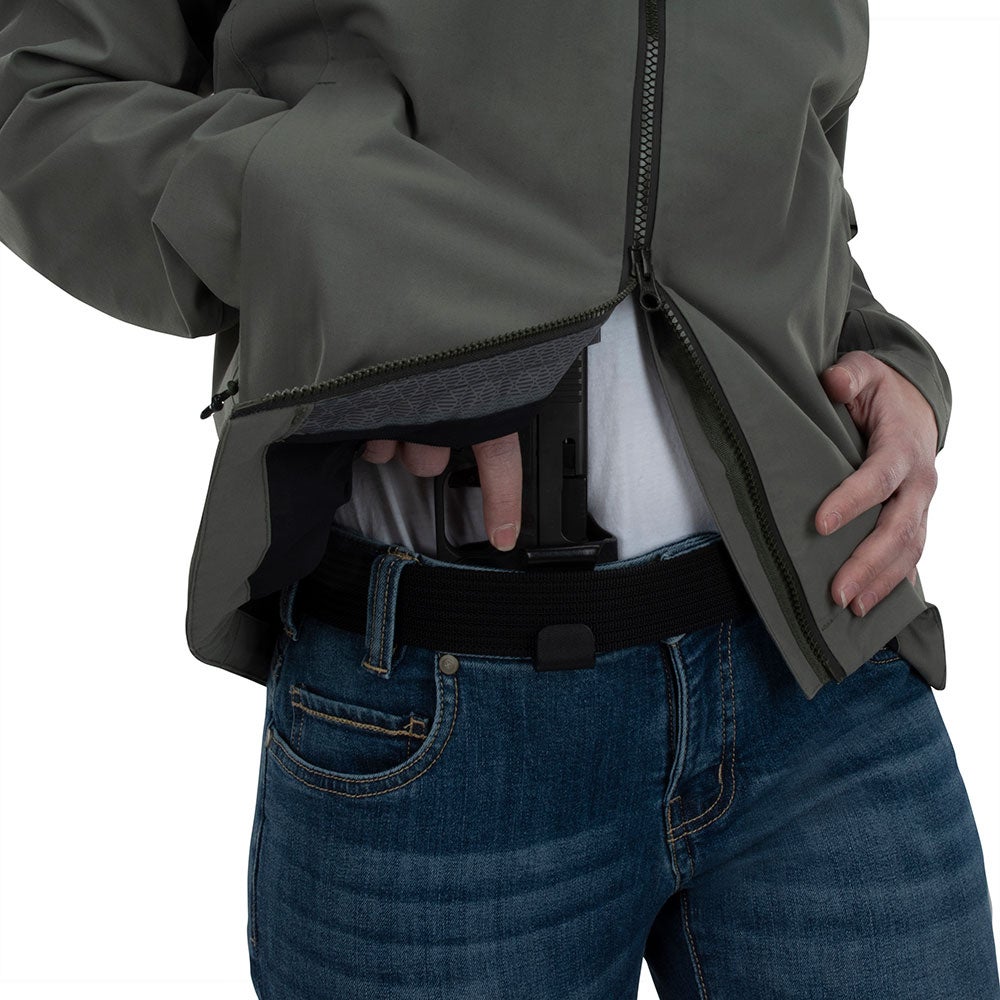 Product shot showing a person drawing a handgun from a concealed waistband holster inside a dark olive green jacket with a black inner lining and blue jeans featuring a visible back pocket