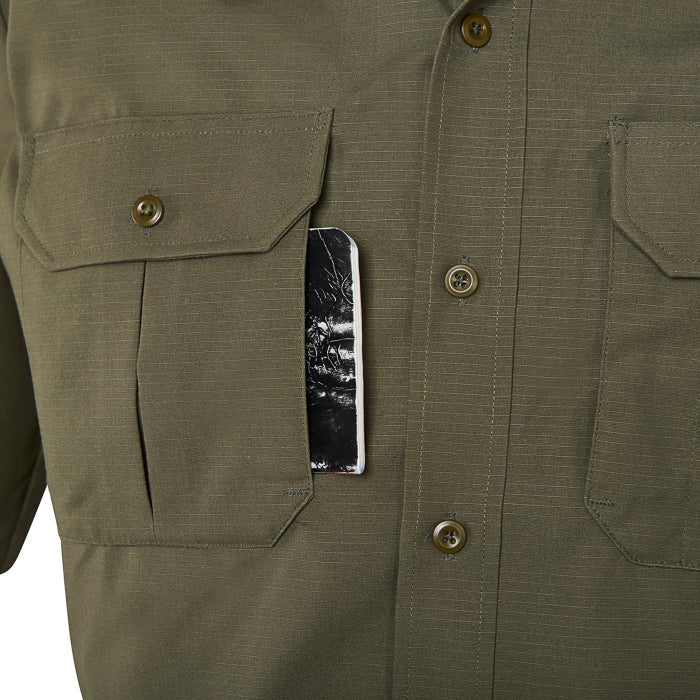 Close-up of an olive green shirt with a pen pocket showing a partially visible notebook with a monochromatic nature scene featuring subtle shading and a hint of red