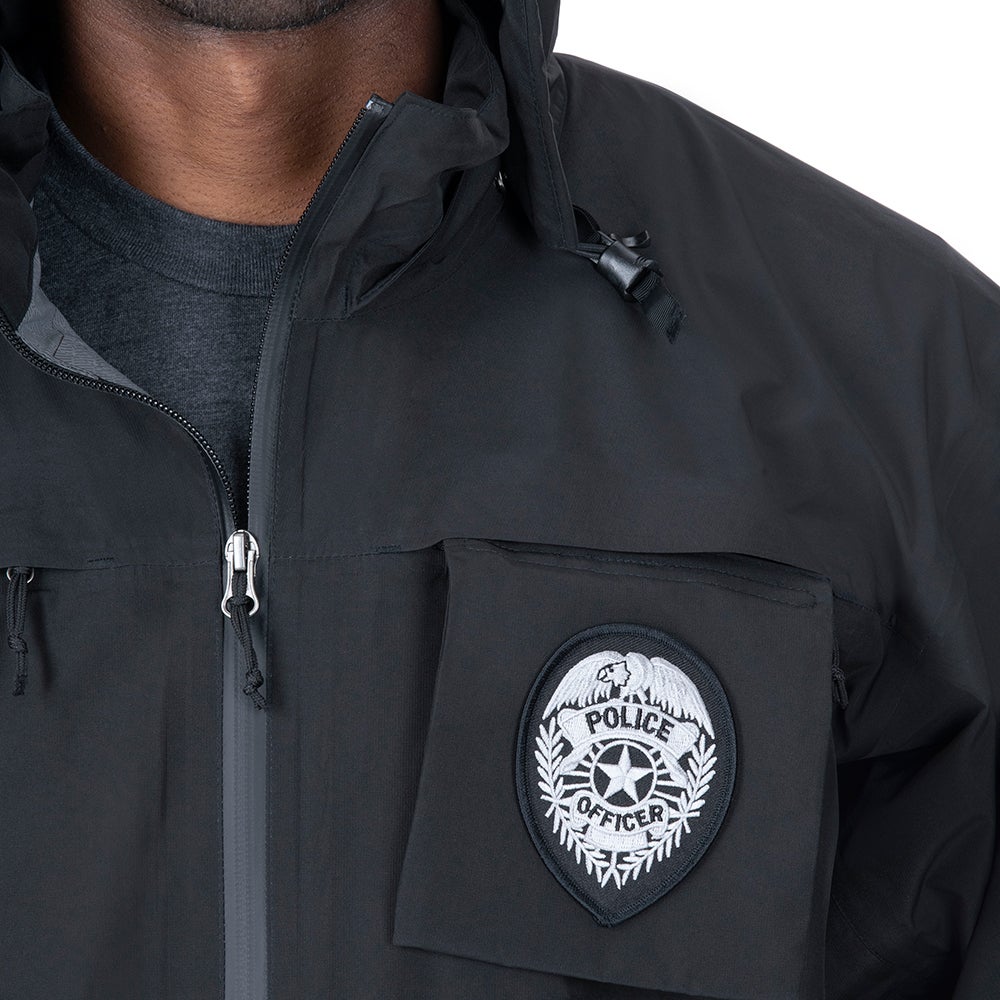 Close-up of a black police jacket featuring a silver police officer badge with an eagle and star detail, a zipper, and a hood.