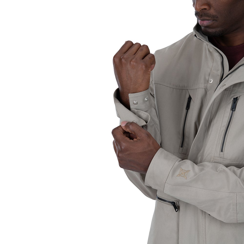 Studio product shot of a man adjusting the cuffs of a light beige jacket featuring adjustable sleeve buttons, zippered pockets, and an embroidered logo on the sleeve
